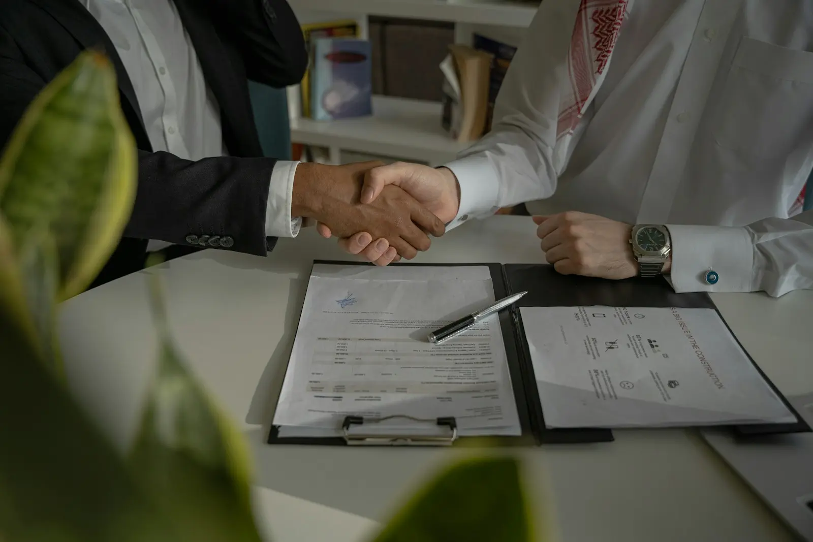 Une poignée de main au-dessus de deux documents posés sur un bureau, avec une plante au premier plan