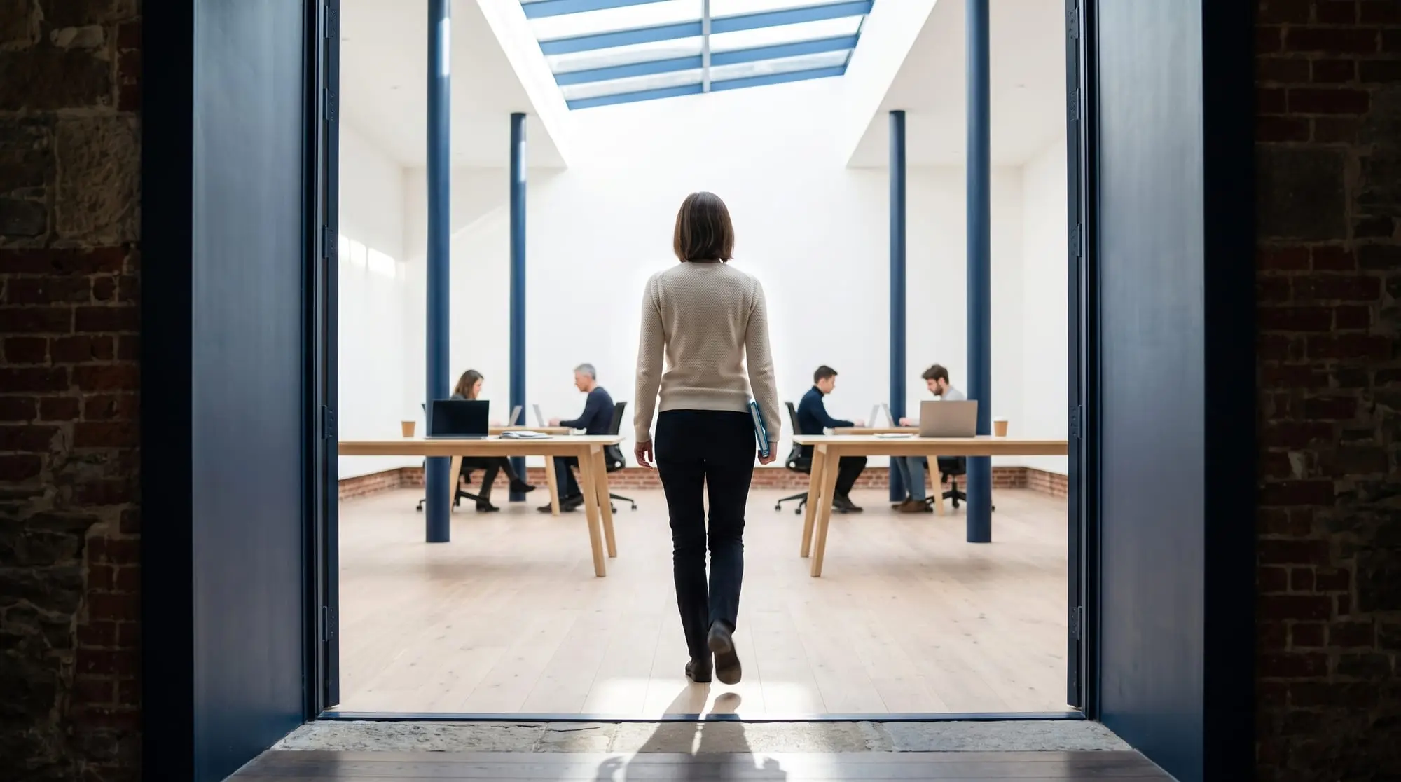 Illustration générée par intelligence artificielle : une personne de dos franchit une haute porte et entre dans un grand plateau lumineux où une équipe travaille