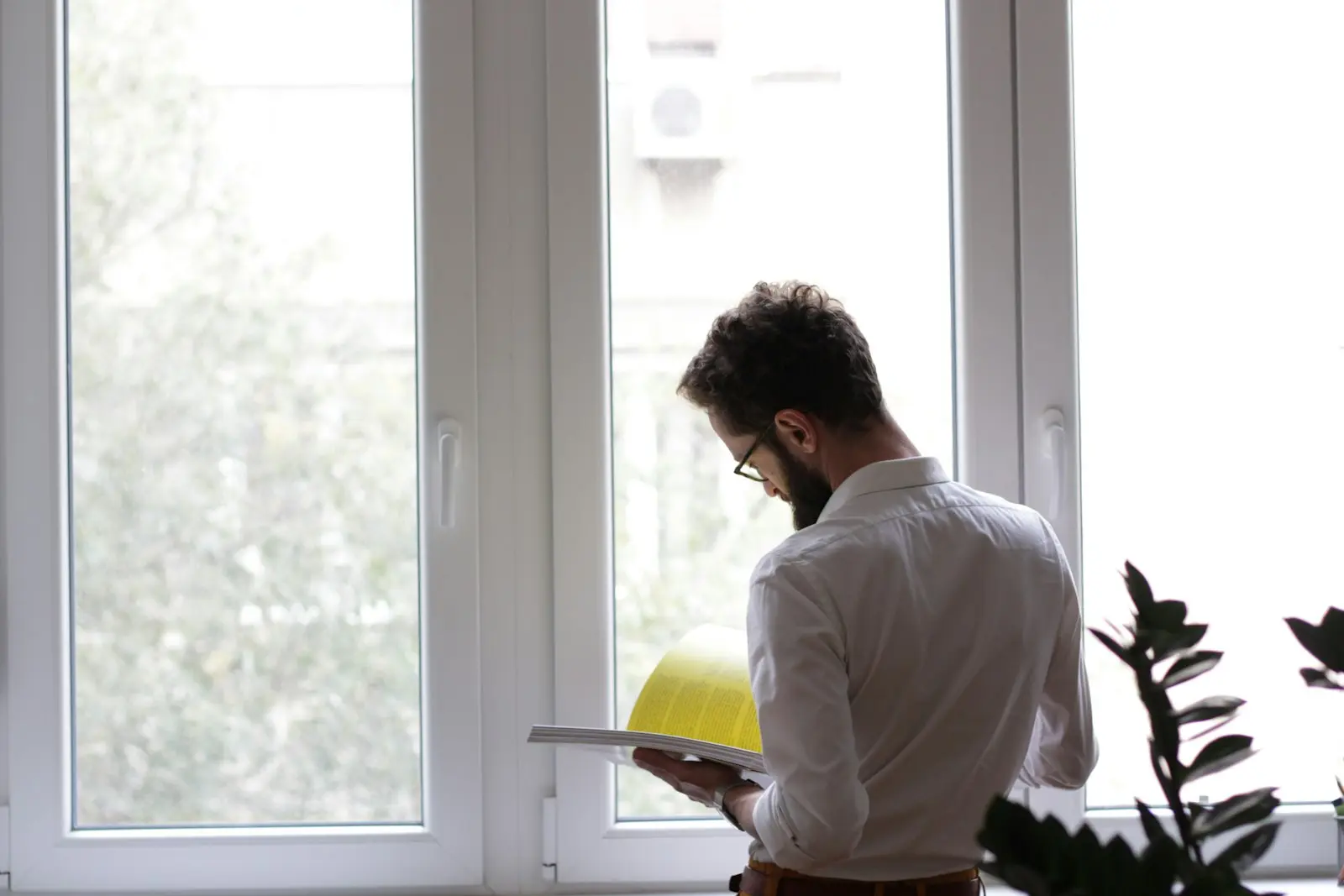 Un homme de dos lit attentivement un document devant une fenêtre