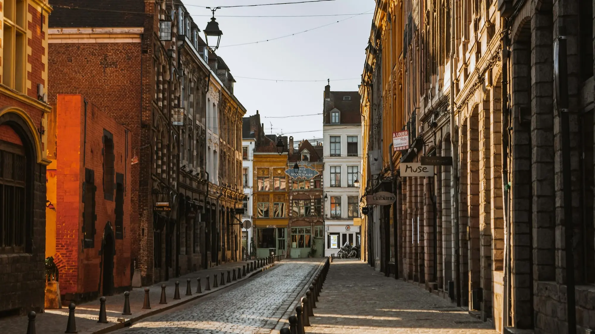 Une rue pavée du Vieux-Lille bordée de façades anciennes, déserte, dans la lumière rasante de fin de journée