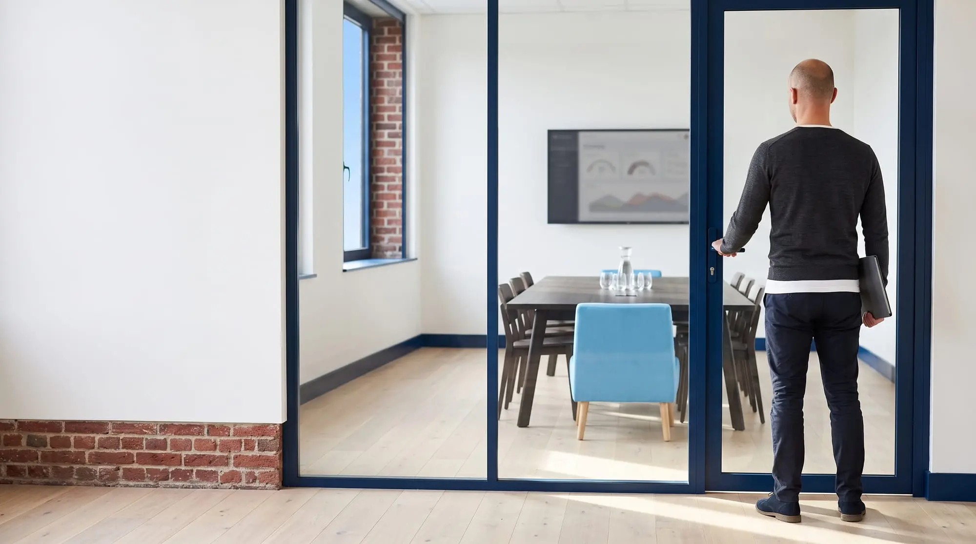 Illustration générée par intelligence artificielle : un homme de dos, la main sur la poignée d'une salle de comité vitrée où la table est dressée et le siège bleu ciel vide