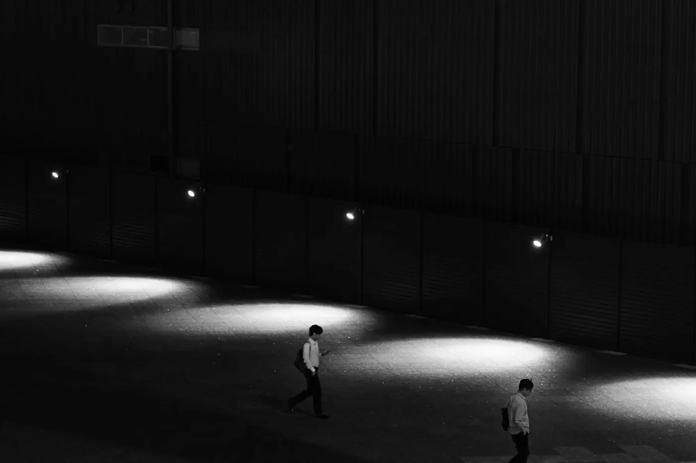 Deux silhouettes traversant un passage sombre, chacune dans son halo de lumière