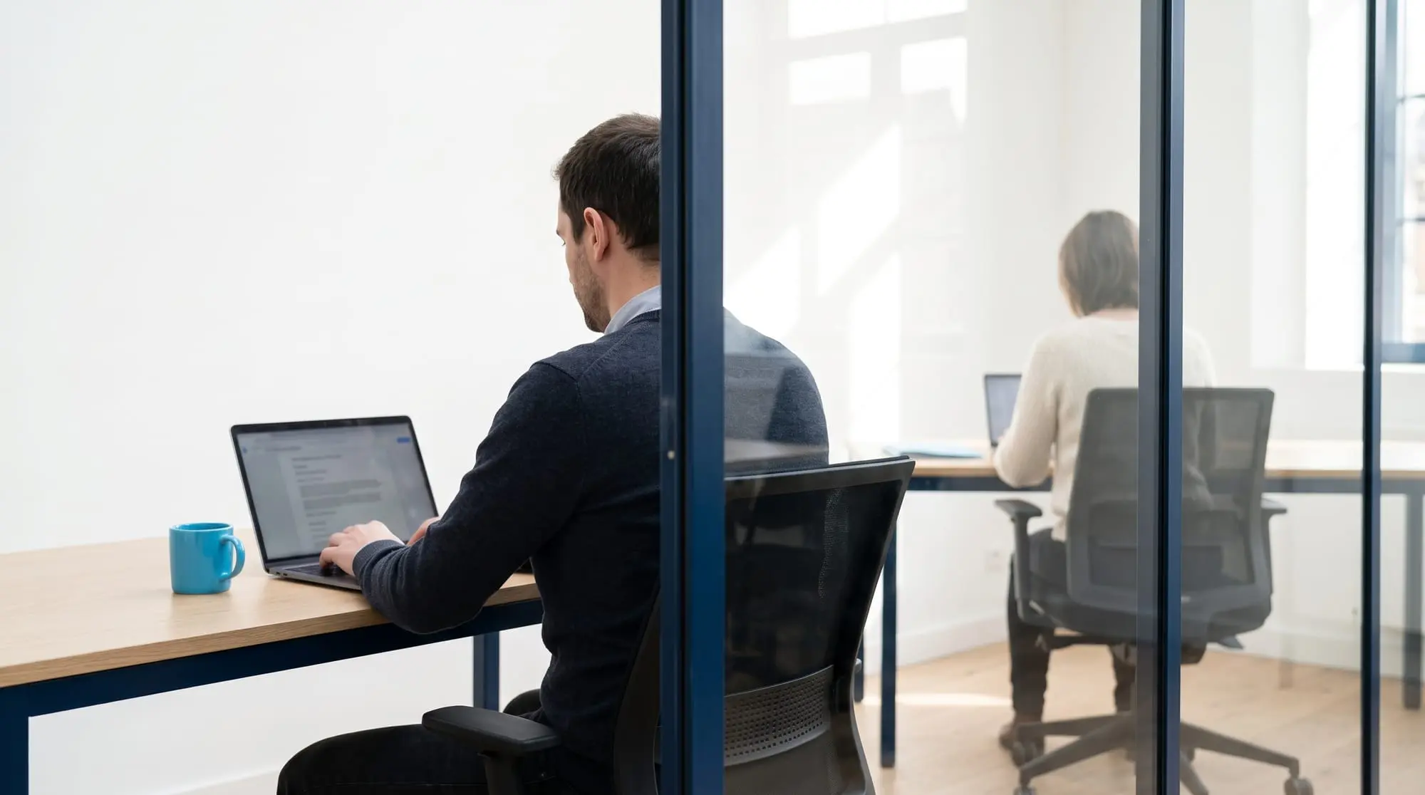 Illustration générée par intelligence artificielle : deux personnes à leur poste de part et d'autre d'une cloison vitrée, dos à dos, séparées par un montant sombre